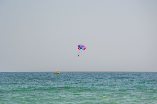 Ocean view of a man parasailing in the sea, towed by speedboat, nature activity outdoors, summer, parasail above water