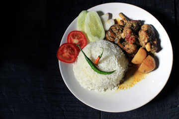 Cup of boiled rice with chicken broth on a white plate isolated on black background. Cooked rice on a white plate, chili, tomato, cucumber