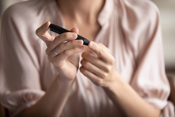 Close up young woman measuring glucose level, blood sugar ranges, using lancet pen on finger,...