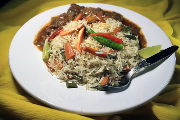 Vegetable fried rice with chili chicken on white plate isolated on yellow cloth. Top view. Chili chicken is a popular Indo-Chinese dish of chicken of Hakka Chinese heritage. 