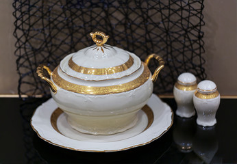 selective focus of salt and pepper shakers with a luxury porcelain tureen with gilding on the table. Close up