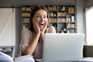 Excited surprised woman looking at laptop screen, reading unexpected good news, getting new job or promotion, funny smiling young female screaming with joy, celebrating online win, feeling amazed