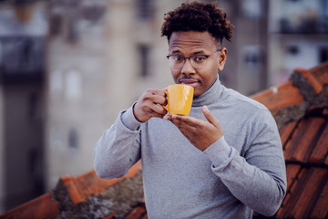 Good-looking african american man standing on rooftop and smelling his fresh morning coffee.