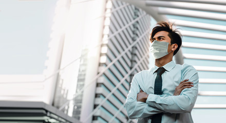 Covid-19 Situation in Business Concept. Businessman with Surgical Mask standing in the City. Protected and Care of Health. Stressed out due to Corona Virus. Looking up into the Sky
