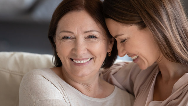 Close up smiling mature mother and daughter hugging, touching heads, expressing love and care, young woman and middle aged mum enjoying tender moment, two generations good relationship