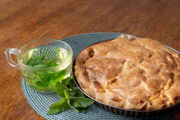 Homemade cake. Apple pie Charlotte.Fresh natural green Melissa herbal tea in a glass Cup. Organic aromatherapy relaxation medical healthy drink. Rustic wooden table background. Rustic style 