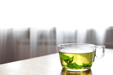 Herbal tea in a glass cup. Tea with fresh mint and Melissa leaves. Glass Cup of invigorating tea on the background of the window. Space for text. Good nutrition.