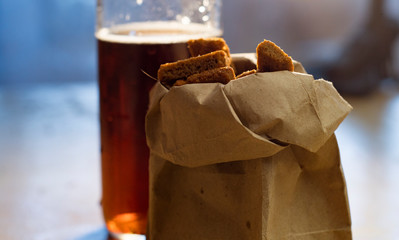 Glass of beer and a paper bag with crackers on the table.