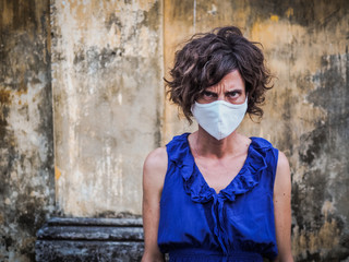 angry and mad woman standing in front of a vintage wall wearing a face mask protecting from corona virus covid-19