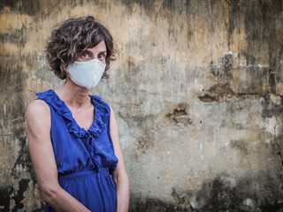sad and disappointed woman standing in front of a vintage wall wearing a face mask protecting from corona virus covid-19 shoulders hanging down