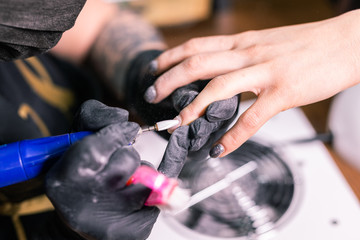 Close-up of manicurist woman removes gel shellac polish from client's nails using manicure machine. Manicure master is working with electric nail drill in beauty salon. Hardware manicure process.