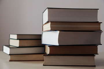 Стопка книг разного размера, на однотонном фоне одна стопка выше чем другая .