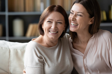 Happy mature mother and adult daughter hugging close up, having fun, sitting on couch at home, smiling woman embracing older mum, spending leisure time together, two generations good relationship - Powered by Adobe