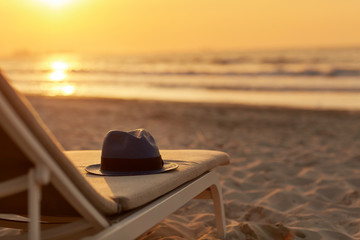 Blue hat is lying on a chaise longue on a beautiful sandy beach by the sea in the rays of the...