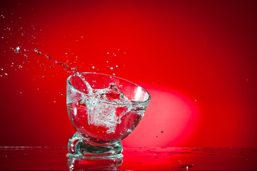 A splash of a drink in a glass, shot against a bright red background.