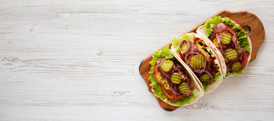 Homemade Bacon Cheeseburger Tacos on a rustic wooden board on a white wooden surface, top view. Flat lay, overhead, from above. Copy space.