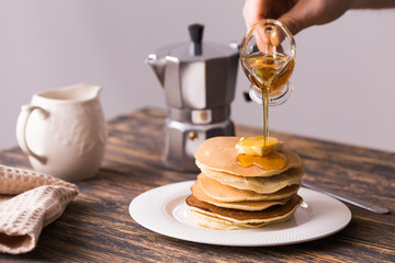 Male hand pouring maple syrup on tasty pancakes.