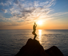 girl is sitting in lotus pose on the big rock in front of sunrise at the sea