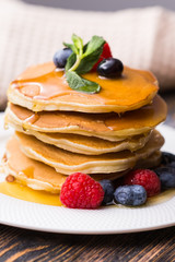 Pancakes with blueberries and raspberry and maple syrup on wooden background. Breakfast and traditional meal.