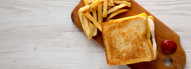Fresh Grilled Cheese Burger with French Fries on a rustic wooden board on a white wooden background, top view. Flat lay, overhead, from above. Space for text.