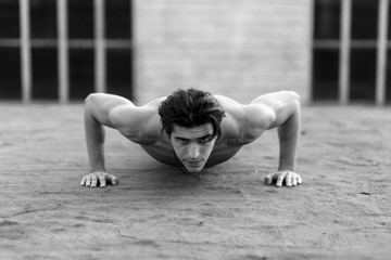 Fototapeta na wymiar Young muscle handsome man does push-ups with naked torso. Black and white image.