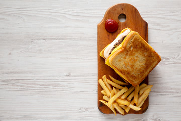Fresh Grilled Cheese Burger with French Fries on a rustic wooden board on a white wooden surface, top view. Flat lay, overhead, from above. Copy space.
