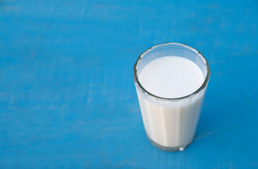 close-up of milk in a faceted glass, a drop flows down the wall. Top view on a blue cyan background, stands on the right side
