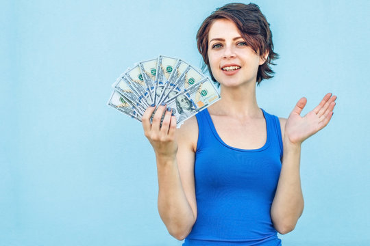 Girl With Money On Blue Background. Happy Funny Young Woman Holding Dollars