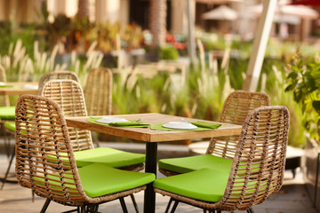 Terrace of a cozy cafe in green tones with wicker furniture under the open sky. Street cafe, street photo