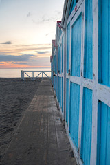Little blue houses on the beach. A place to store beach utensils. Rasset (sunset) on the Mediterranean coast. The concept of a relaxing beach holiday. Old cracked paint