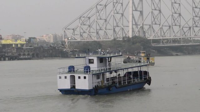 A boat carrying Passenger ferry service station by West Bengal Shipping Surface Transport Corporation (WBSTC) on Ganges river connecting Kolkata and Howrah city. Howrah bridge at a distance. India 
