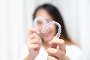 Women hand hold inivisalign braces, transparent aligner, invisible retainer or orthodontic silicone trainer with blur mile in background. A way to have a beautiful smile.