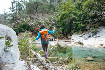 A woman with a backpack crosses a river on a log.