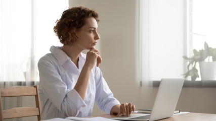Thoughtful young female doctor thinking of medical question at workplace. Serious doubtful woman...