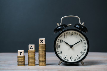 Time to pay TAX concept. TAX alphabet with stack of coin and vintage alarm clock in dark background, business and financial concept idea.