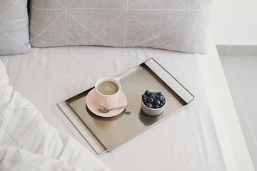 Breakfast in bed concept. Coffee with milk in a pink cup and fresh blueberry on a metal tray. Morning coffee