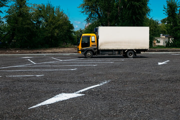 small truck with a yellow cab and a white one-trailer in a parking lot with direction arrows
