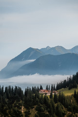 Germany Bavaria Nature Alps Mountains. In the mountains against the sky, fog and green forest stands a house in the distance. Alpine houses, hotel. Summer. House among the mountain landscape