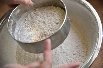 Female cook in apron sifts flour in a metal bowl. Preparing to create a dough for baking. Homemade Patisserie.