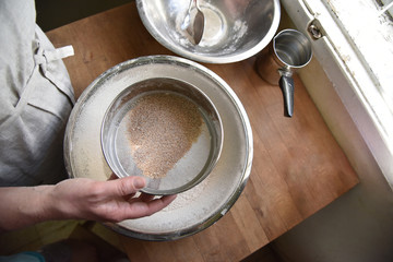 Female cook in apron sifts flour in a metal bowl. Preparing to create a dough for baking. Homemade Patisserie.