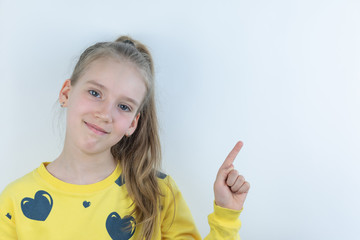 Workpiece or template with beautiful, nice, cool and pretty young girl or child in yellow T-shirt on white showing domonstrating something behind her on background by means of her hand as presentation