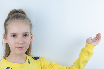 Workpiece or template with beautiful, nice, cool and pretty young girl or child in yellow T-shirt on white showing domonstrating something behind her on background by means of her hand as presentation