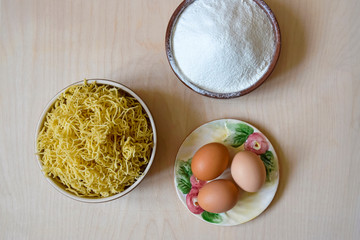 Cooking homemade noodles, flat lay. Raw pasta.On wooden surface are wheat flour, eggs on plate and finished product. Top view. Copy space.