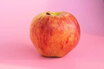 Red yellow apple on a pink background. Juicy ripe beautiful fruit.
