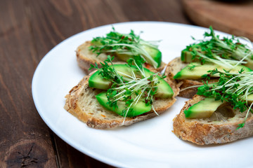 sandwiches with avocado and microgreens on a white plate close-up. healthy breakfast option.