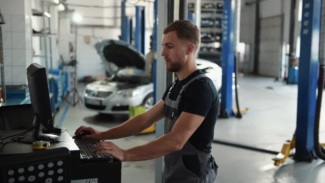 Man at the workshop in uniform use computer for his job for fixing broken car.