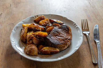 Sirloin Steak of Black Angus beef with potato wedges on a white plate on dark wooden table with fork and knife