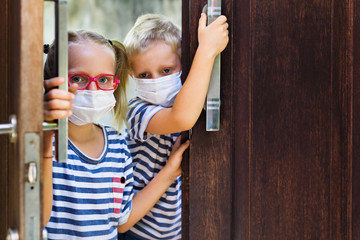 Little children looking unhappy and depressed after staying at home due banned street activity. Kids wearing medical face masks go out for outside walk, ending coronavirus Covid-19 disease quarantine.