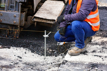 A worker with a stretched thread sets the necessary level for the subsequent asphalting of a new section of the road.