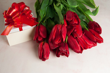 Flower composition. A bouquet of spring red tulips, a gift box with a large bow and a paper blank on a pink marble background. Selective focus.